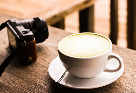 A cup of coffee or tea and the mirrorless camera on the wood table at the balconyの写真素材