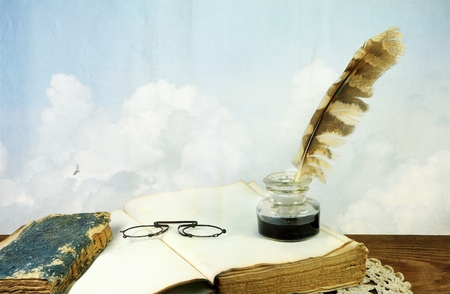 Desk with old books, pince-nez and inkwell on background of skyの写真素材