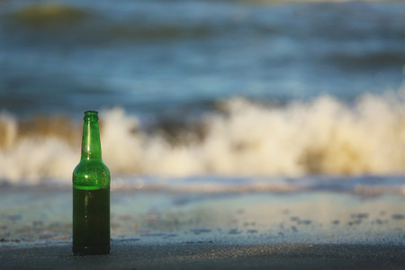 Green beer bottle sitting in the sand on the seashore.の写真素材