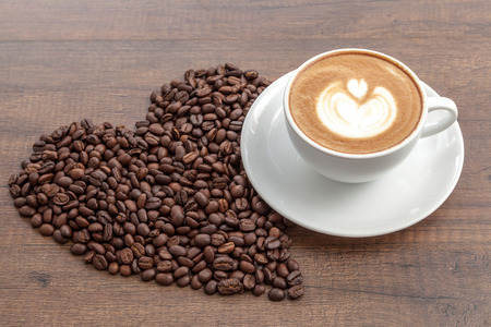 Coffee cup of latte art with coffee beans in heart shape on wooden background