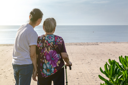 Mother and daughter stand together in front of the beach looking at the sea.  This shows the warmth love in family. This can be related with any article about family, elder, health.の写真素材