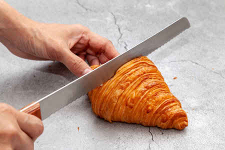 Sliced fresh baked croissant with bread knife on cement background.の写真素材