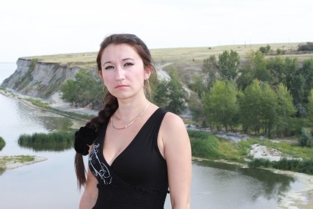 Serious girl standing on background of the water landscapeの写真素材