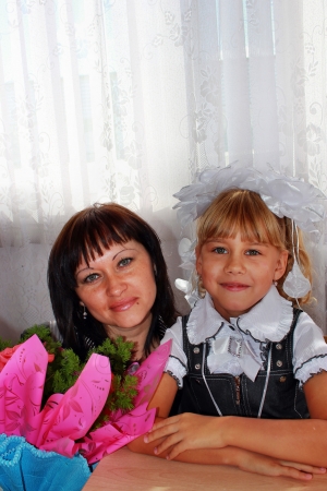 First grader girl sitting at a desk with his mother, with a bouquet of flowersの写真素材