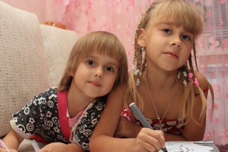 Smiling sisters draw together, lying on the couchの写真素材