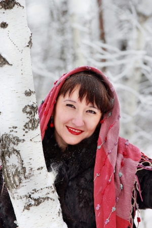 A smiling girl in a pink scarf, stands near the birch trees in winter forestの写真素材
