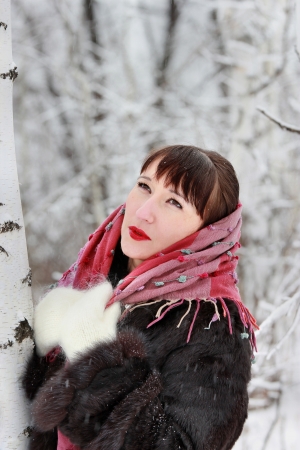 Beautiful woman in winter forest near birch, looks upの写真素材