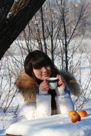 A young girl sitting at a table in a winter forest, drinking teaの写真素材