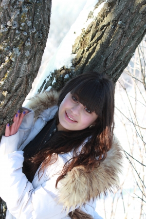 A girl in a white jacket, standing near a treeの写真素材