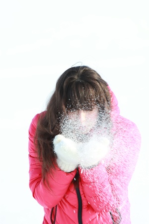 A young girl in a pink jacket blows away the snow from handsの写真素材