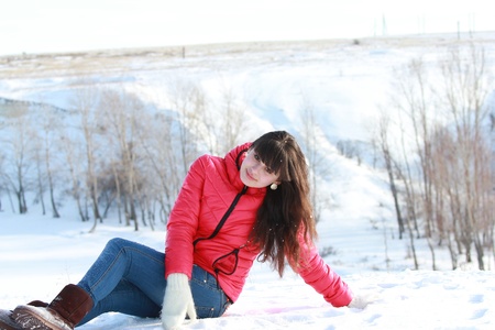 A girl in a pink jacket on the fresh air, sitting on the white snowの写真素材