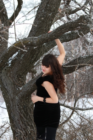 A young brunette in a black dress in the woods near a treeの写真素材
