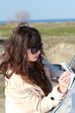 Business girl in sunglasses, writes in a notebook near the carの写真素材