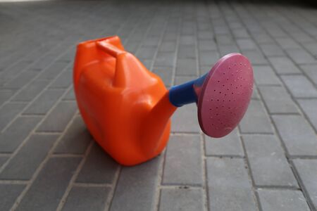 garden watering can of orange color with a claret tip costs on a tile.の写真素材