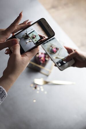 two girls with phones in hands take the picture of beautiful piece of cake	