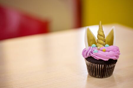 Chocolate cupcakes with pink icing decorated in the shape of a unicorn, Golden ears and horn. delicious pastries on the table.の写真素材