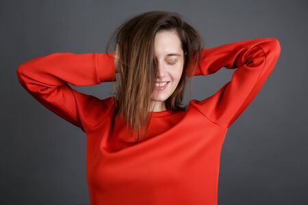 cheerful beautiful young woman in a red jacket. brunette on a dark gray background in the Studio. a smile on her face and her hair covered half her face.の写真素材