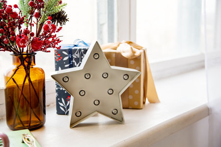 a white star with light bulbs on the windowsill against the background of gifts and with a brown...