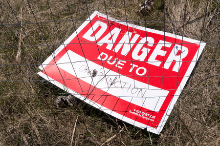danger due to construction red sign left on dry grass ground behind  wire netting