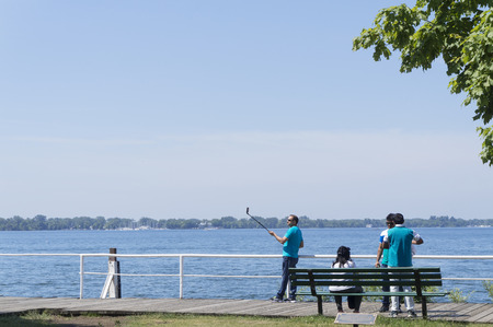 A boardwalking tourist takes a selfie in front of the Lake Ontario on a sunny day. The Lake Ontario is one of the top Ontario tourist attractions.のeditorial素材