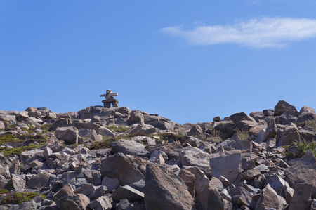 A delicately balanced inukshuk or cairn on top of stone hill against blue sky.の写真素材