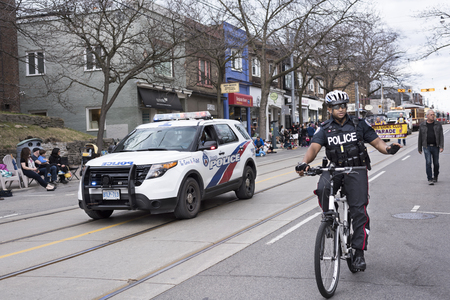 a policeman, followed by a police car, cycles at the beginning of the Easter Parade procession and waves to people along the Beaches Queen streetのeditorial素材