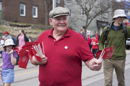 an old man in red t-shirt distributes Canada 150 flags to people along the Queen Street East in the Beaches Easter Parade 2017.のeditorial素材