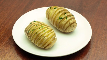 Hasselback Potatoes Sprinkled with Dill - Traditional Swedish Sliced Baked Potatoes on White Plate