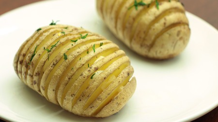 Hasselback Potatoes Sprinkled with Dill - Traditional Swedish Sliced Baked Potatoes on White Plate
