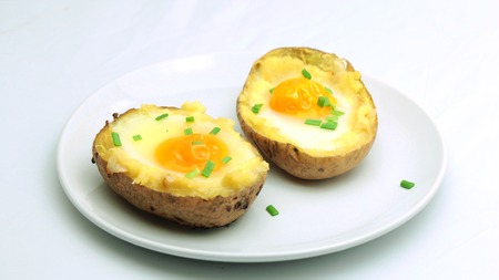 Twice baked potatoes with egg on top on white plateの写真素材