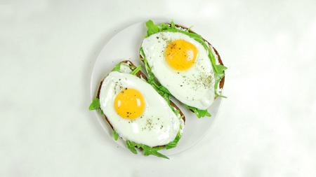 Open avocado, egg sandwiches on whole grain bread on a White Plate on a White Background.