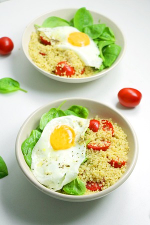 Savory Breakfast Quinoa with Spinach, Tomatoes and Fried Eggs. Healthy Food on a White Backgroundの写真素材