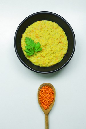 Healthy lentil porridge topped with parsley in a black bowl on a white tableの写真素材
