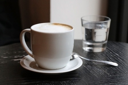 Latte coffee in a white cup on old wooden table with glass of water and spoon.