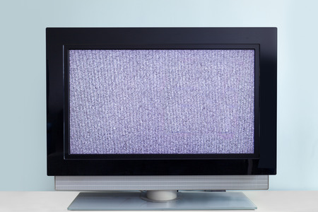 Modern LCD TV with signal noise, against blue wall
