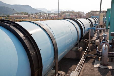 Large water pipe in a sewage treatment plant with digestion tanks in the background