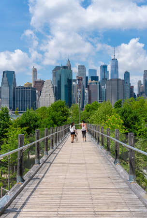 New York, USA - May 21, 2018: People walking on an elevated walkway towards the Brooklyn Bridge Park, with New York skyline in the backgroundのeditorial素材