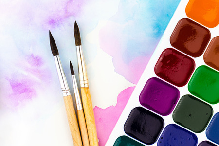 A palette of watercolor paints, brushes and paper for watercolors with colored spots. Flat lay...