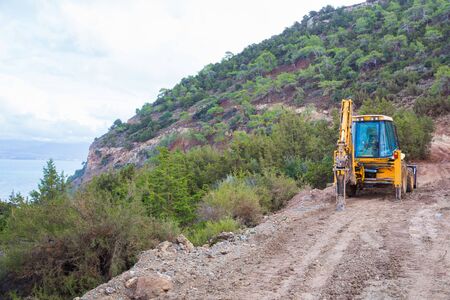 City Paphos, Cyprus. Yellow excavator on the hill, dirty way. Urban view. Travel photo 2018, december.のeditorial素材