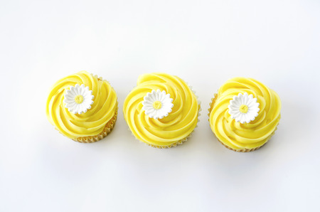 Three yellow cupcakes with daisy decorationの写真素材
