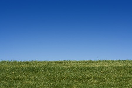 A horizontal photo of a grassy hill with clear blue sky behind it. Lots of room for copyの写真素材