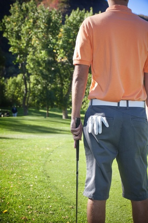 A rear view photo of a golfer standing around the green of a golf courseの写真素材