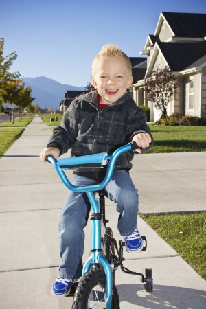 Little boy learning to ride a bike with training wheelsの写真素材