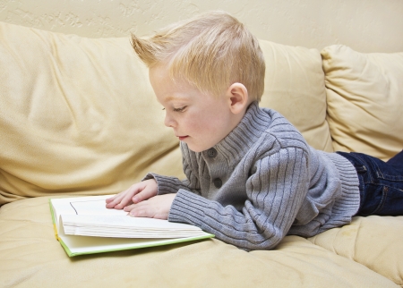 Cute boy reading a book on the couchの写真素材
