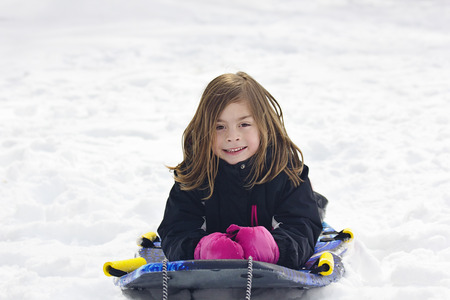 Cute Little Girl going snow sledding down a hill
