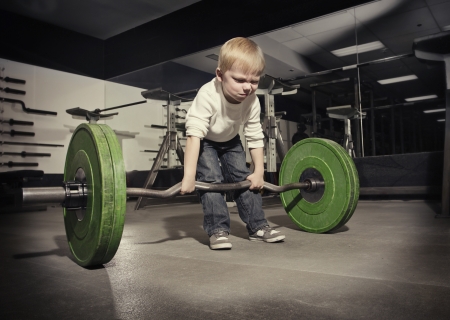 Determined young boy trying to lift a heavy weight bar