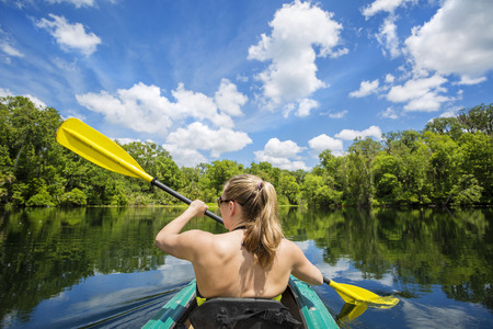 Woman kayaking along a beautiful tropical jungle river. Lots of copy space above and view from behindの写真素材