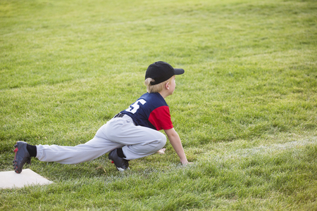 Young boy baseball player waiting on third base. He showing a funny sprinters stance