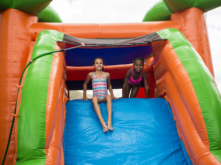 Happy little girls sliding down an inflatable bounce houseの写真素材