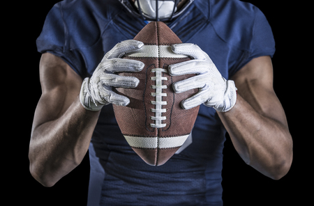 Close up view of an American Football player holding a football. Selective focus on the laces of the football and the wide receiver gloves. Shot on a black backgroundの写真素材